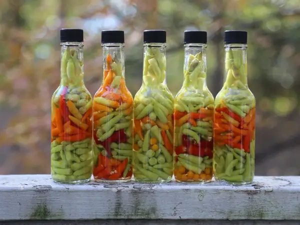 Bottles of Louisiana pepper sauce filled with pickled peppers on a weathered rail