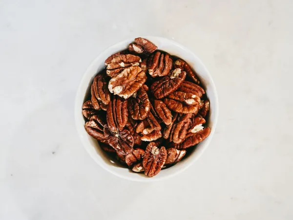 A white bowl of shelled Louisiana pecans on a pale stone counter