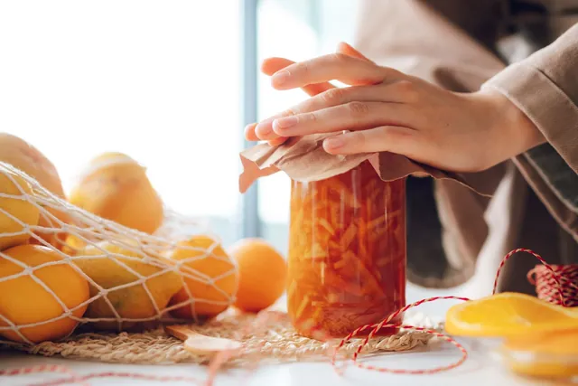 A jar of freshly made satsuma marmalade beside whole citrus on a kitchen counter